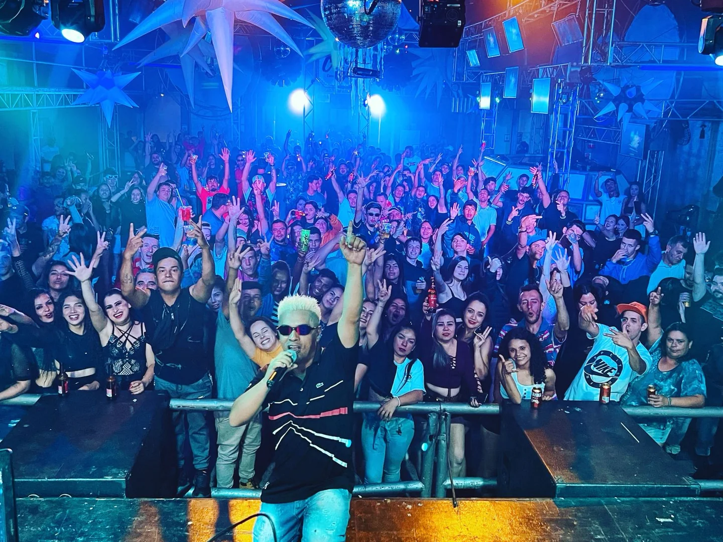 MC Jair da Rocha com microfone no palco e público ao fundo, sob luzes azuis